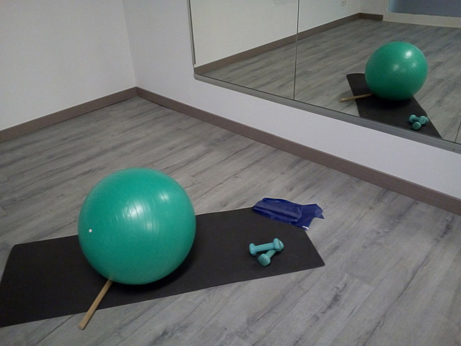 Esterilla centrada en el suelo junto a una pelota de pilates y pesas
