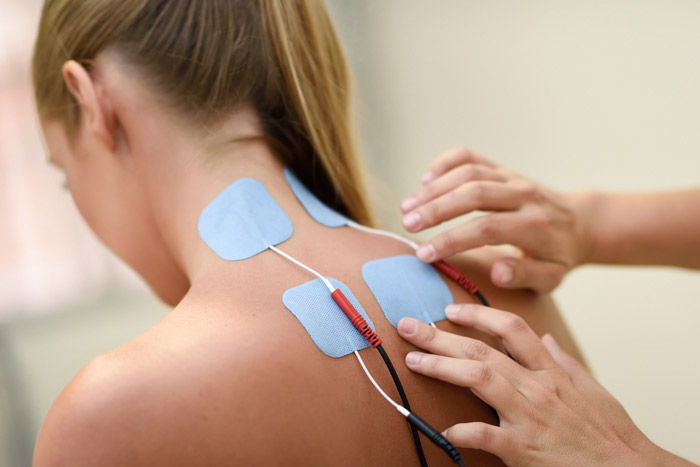 Mujer joven de espaldas que le ponen nodos de electroterápia